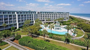 Un hotel de varios pisos con área de piscina, rodeado de palmeras y vistas a la playa.