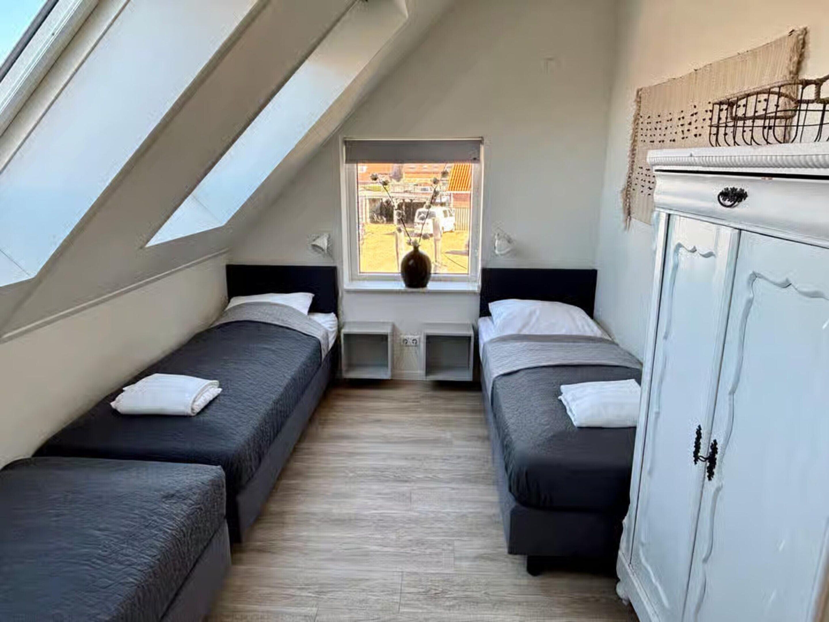 A dormitory room with two beds, a window with a view of the street, a small table, and a wardrobe.