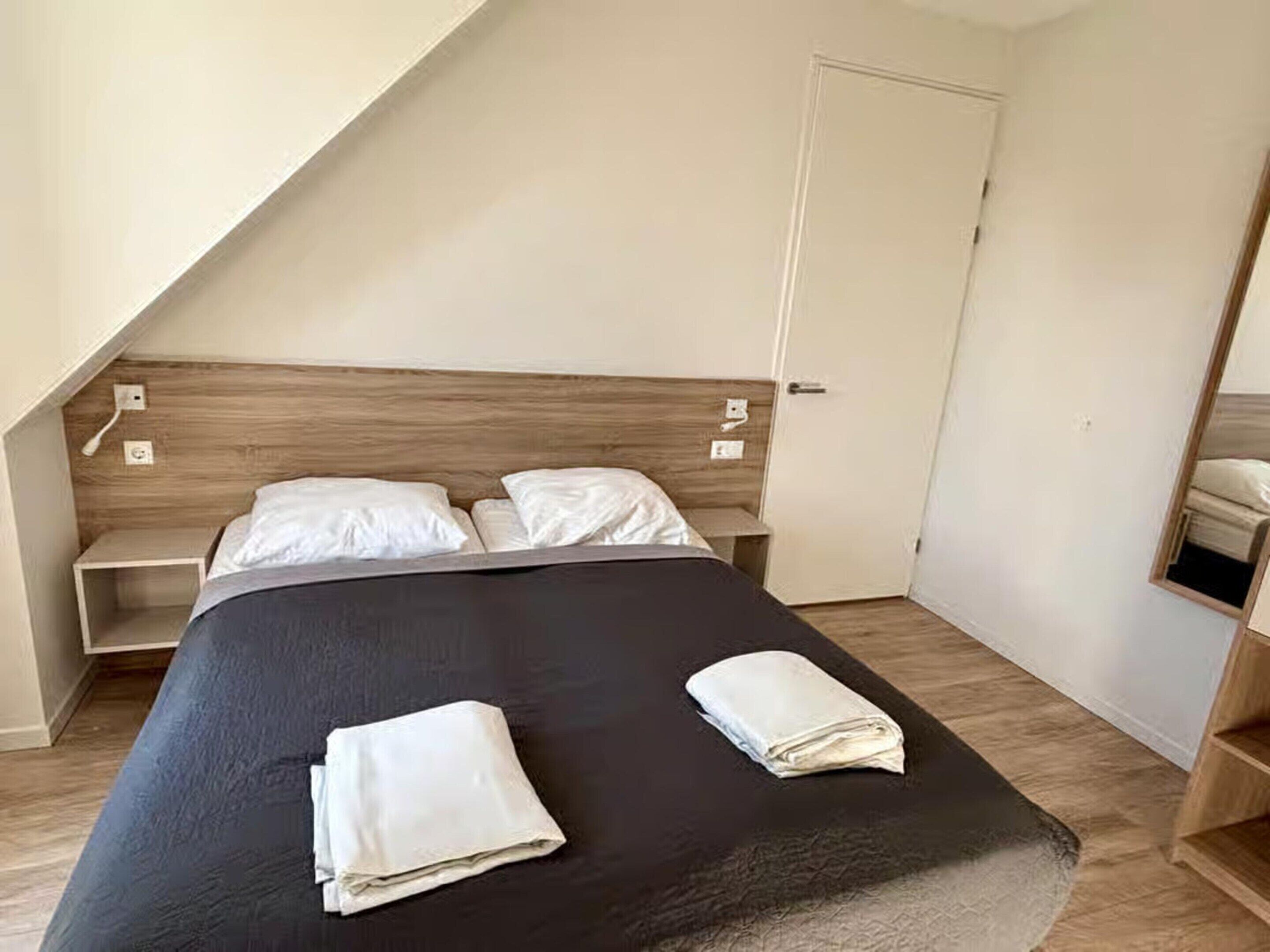 A bedroom with a bed, two pillows, a bedside table, and a wooden headboard.