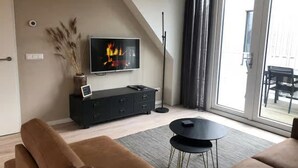 A modern living room with a flat-screen TV, a black entertainment unit, a sofa, and a dining table. - 5-person Lodge With Private Balcony (Zoutelande)