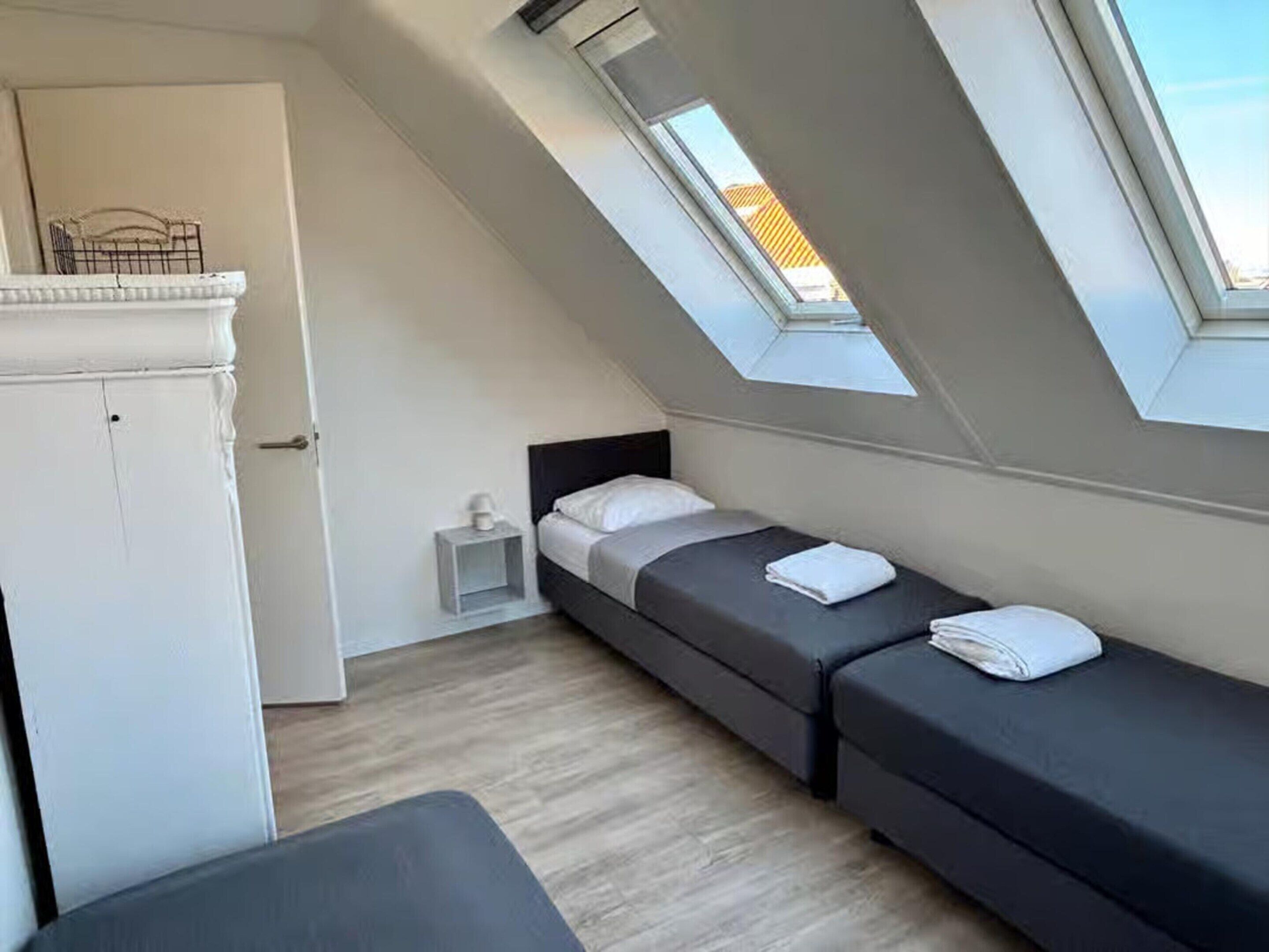 A small, modern room with a sloped ceiling and skylights, featuring two beds and a small white cabinet.