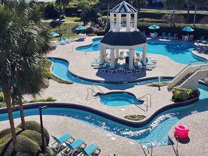 Un área de piscina con varias piscinas, sillas de descanso y un pabellón.