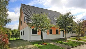Ein modernes, zweistöckiges Haus mit Schrägdach, umgeben von einem gepflegten Garten und Bäumen.