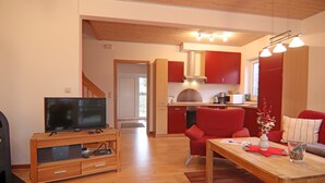 Ein modernes Wohnzimmer mit Fernseher, Holzmöbeln und einem roten Sessel.