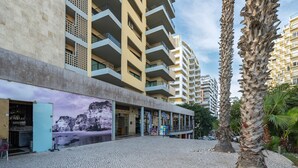 A multi-story building with balconies, a cobblestone plaza, and palm trees. - Apartment 'Ocean Horizon House' with Sea View, Wi-Fi and Air Conditioning (Portimão)