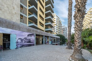Ein mehrstöckiges Gebäude mit Balkonen, einem Kopfsteinpflasterplatz und Palmen.