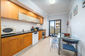 A modern kitchen with wooden cabinets, a microwave, a dishwasher, and a glass dining table with chairs. - Apartment 'Ocean Horizon House' with Sea View, Wi-Fi and Air Conditioning (Portimão)