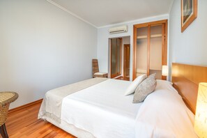A bedroom with a bed, a chair, a lamp, and a wooden wardrobe. - Apartment 'Ocean Horizon House' with Sea View, Wi-Fi and Air Conditioning (Portimão)