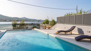 A swimming pool with lounge chairs, a view of the sea, and a distant cityscape. - Seaside Villa With Swimming Pool in Barotul (Pasman)