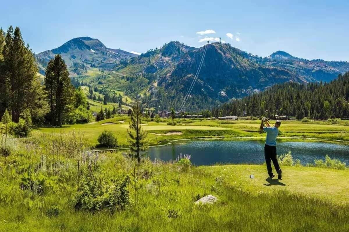 A person fishing by a lake with mountains in the background.