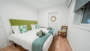 Une chambre avec deux lits, une tête de lit verte et une chaise en bois.