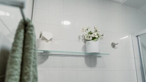 Une salle de bain aux carreaux blancs, une étagère en verre ornée d’un vase de fleurs et une serviette accrochée au mur.