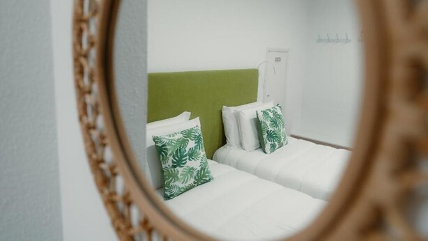 Une chambre d’hôtel avec deux lits, du linge de lit blanc, des oreillers à motifs de feuilles vertes et une tête de lit verte.