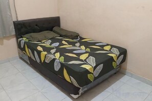 A single bed with a dark headboard and a floral bedspread in a room with plain walls and tiled flooring. - Homestay Komodo Mountain View (Batu Cermin)