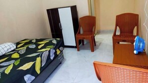A small room with a bed, two wicker chairs, a wooden table, and a blue fan. - Homestay Komodo Mountain View (Batu Cermin)