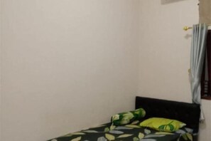 A small, single-bed room with a plain wall and a window with curtains. - Homestay Komodo Mountain View (Batu Cermin)