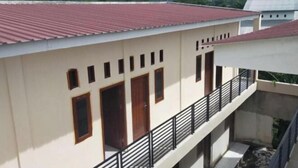 A building with a red roof, beige walls, and a balcony with a black railing. - Homestay Komodo Mountain View (Batu Cermin)