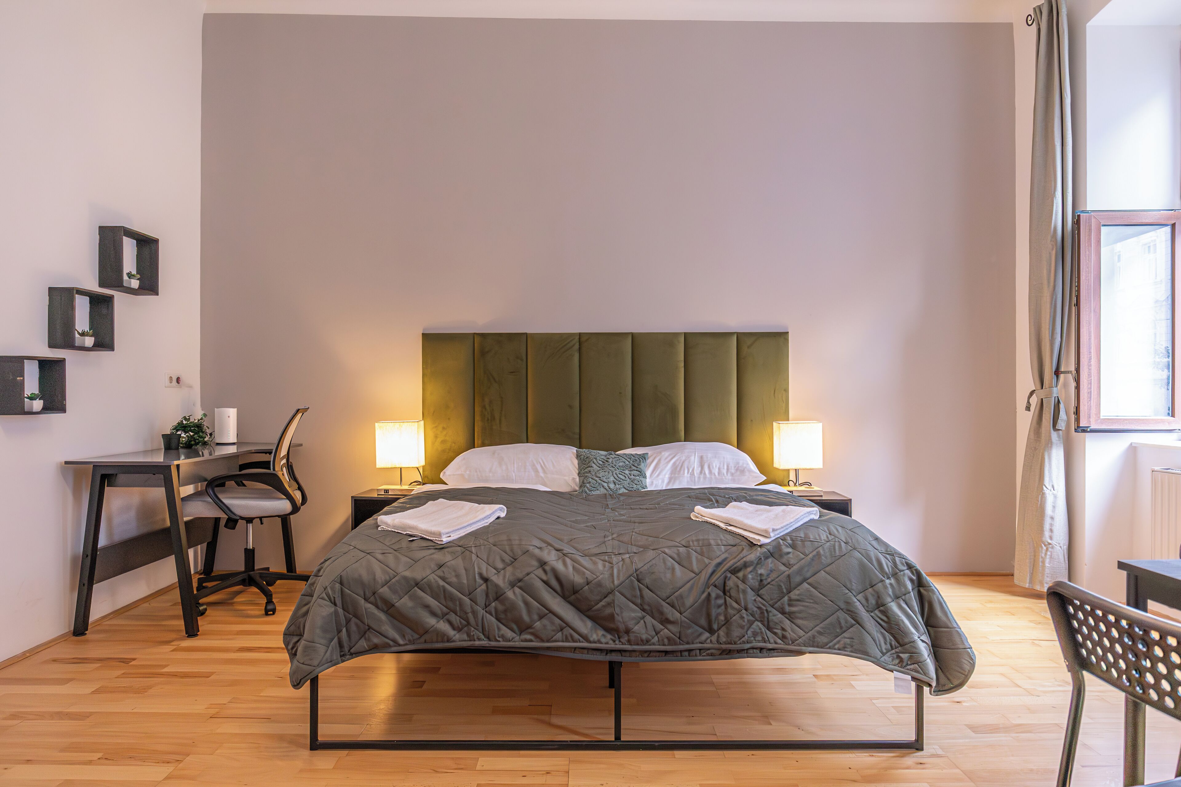 Een keurig opgemaakt slaapkamer met een bed, nachtkastjes, een bureau en een stoel.