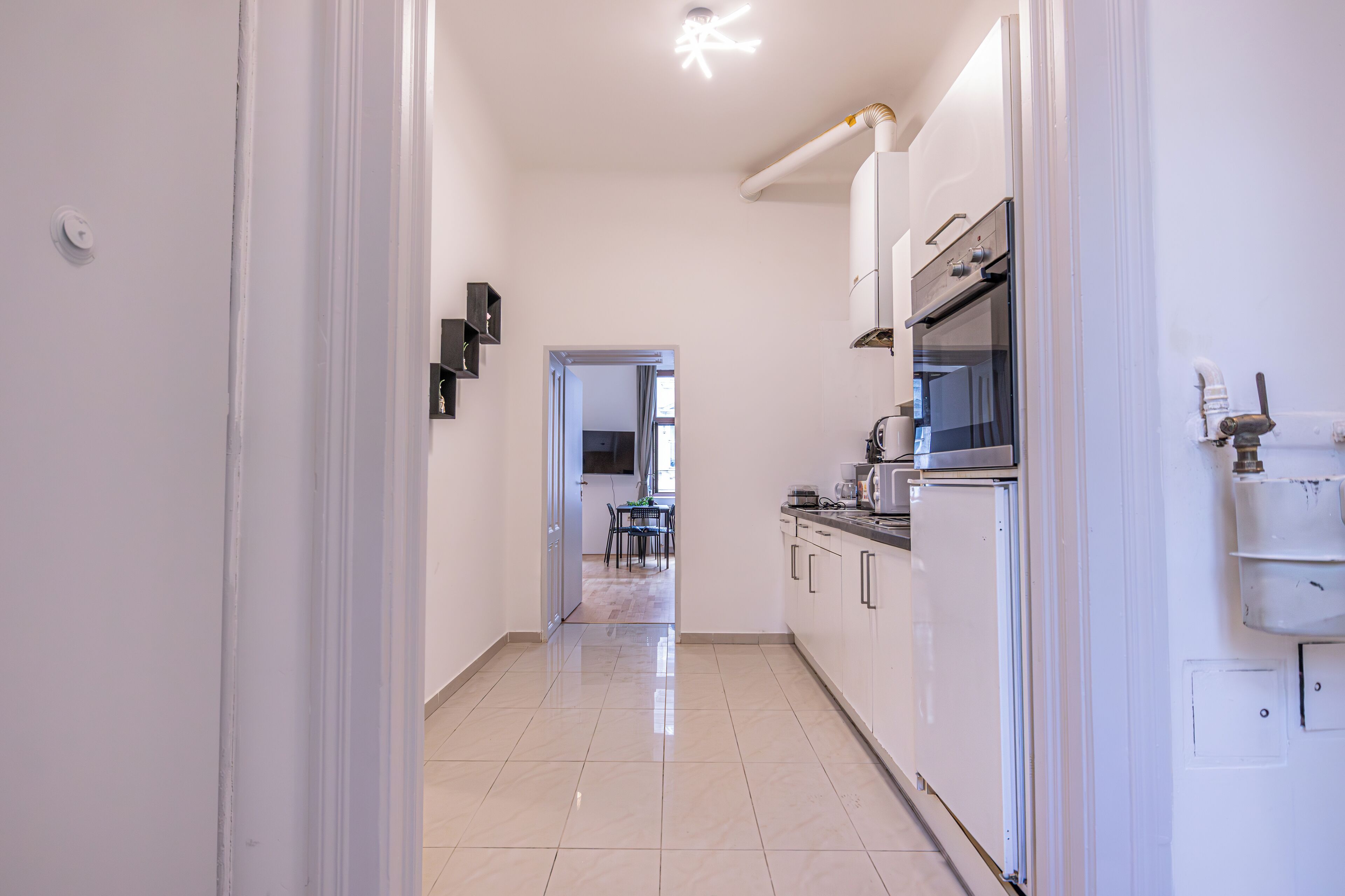 A modern kitchen with white cabinets, a stainless steel oven, and a dining area visible through an open doorway.