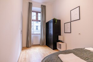 A bedroom with a bed, a wardrobe, a bedside table with a lamp, and a window with curtains. - Affordable 2BR Apartment in Vienna (Vienna)