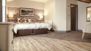Une chambre à coucher avec un lit, deux lampes de chevet, un radiateur, un plancher en bois, une porte et une chaise.