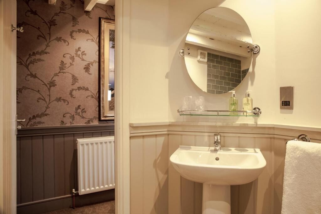 A bathroom with a white sink, a glass shelf above it, and a round mirror.