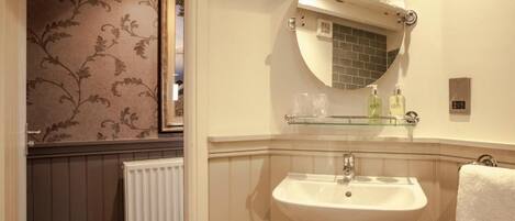 A bathroom with a white sink, a glass shelf above it, and a round mirror.