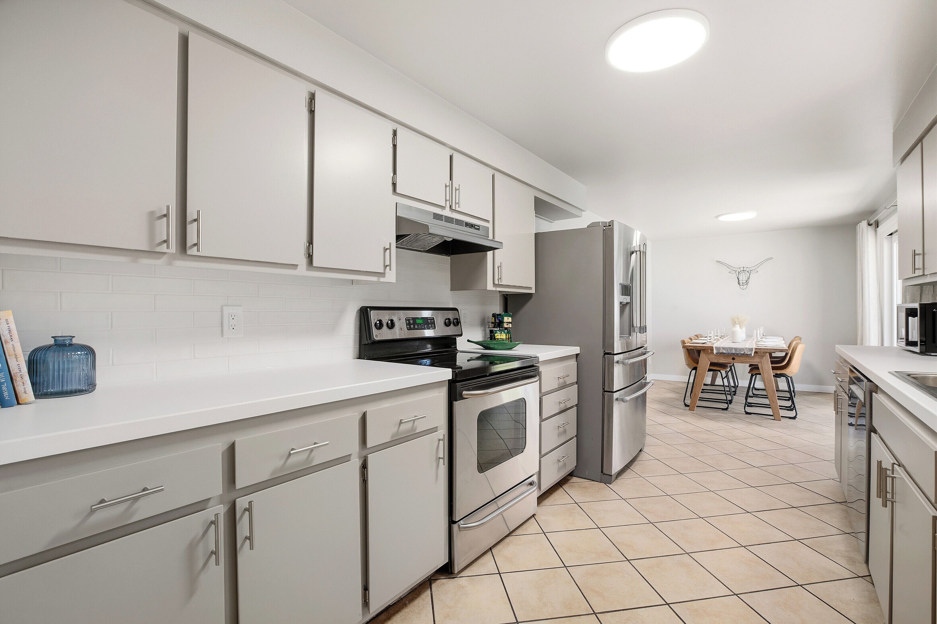 Una cocina moderna con armarios blancos, electrodomésticos de acero inoxidable y piso de baldosas.