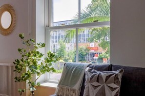 Ein Zimmer mit einem großen Fenster, einer Zimmerpflanze und einem Sofa mit einer Decke.