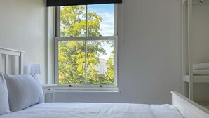 Une chambre avec une grande fenêtre, un lit, une table de chevet et une lampe.
