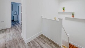 Un intérieur moderne avec des murs blancs, un plancher en bois et un escalier doté d’une rampe blanche.