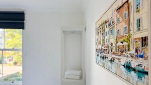 Une pièce dotée d’une grande fenêtre, d’une porte et d’une œuvre d’art fixée au mur représentant une scène de canal.