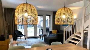 A modern living room with a wooden dining table, two blue chairs, a black sofa, and a staircase. - Beautiful Lodge for 5-person Near the Beach (Zoutelande)
