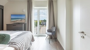 A hotel room with a bed, a chair, a TV, and a large window with curtains. - Luxusapartement mit Meerblick (Nordstrand)