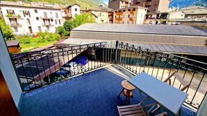 A balcony with a table and chairs, a view of a mountainous area, and a building with balconies. - Bernina Stop & Go apartment - 30 steps to the red train (Tirano)