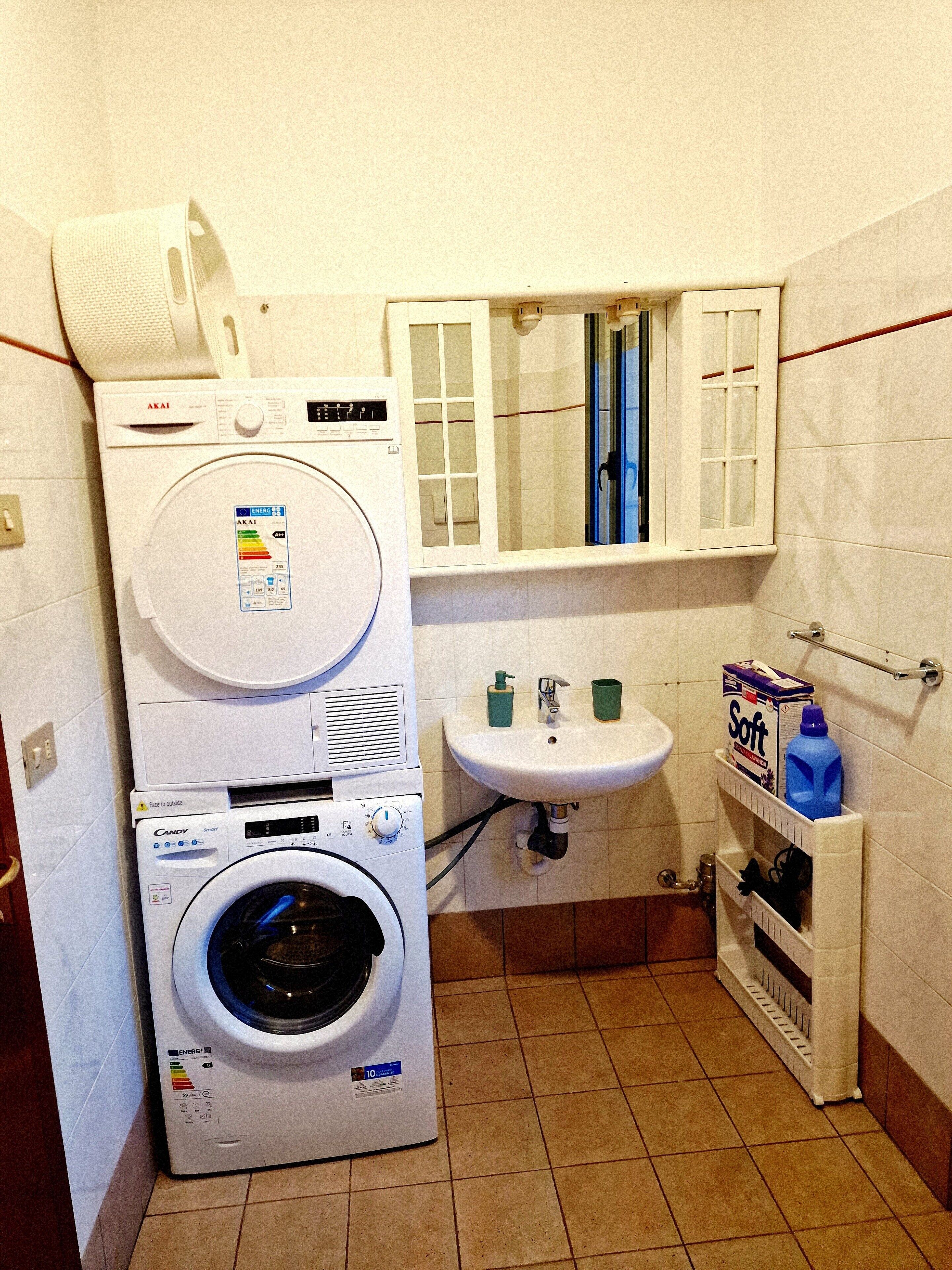 A compact laundry room with a front-loading washer and dryer, a sink, and a medicine cabinet.