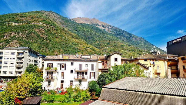 A residential area with multi-story buildings, a small garden, and a mountain in the background. - Bernina Stop & Go apartment - 30 steps to the red train (Tirano)