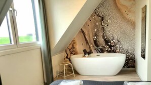 A modern bathroom with a freestanding bathtub, a small stool, and a large window. - Beautiful Lodge Parallel to the Shopping Street (Zoutelande)