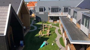 A residential area with modern houses, a green lawn, and a children's play area with a slide. - Beautiful Lodge Parallel to the Shopping Street (Zoutelande)