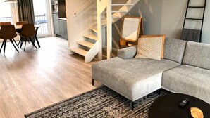 A modern living room with a grey sofa, a staircase, and a dining area with chairs and a table. - Beautiful Lodge Parallel to the Shopping Street (Zoutelande)