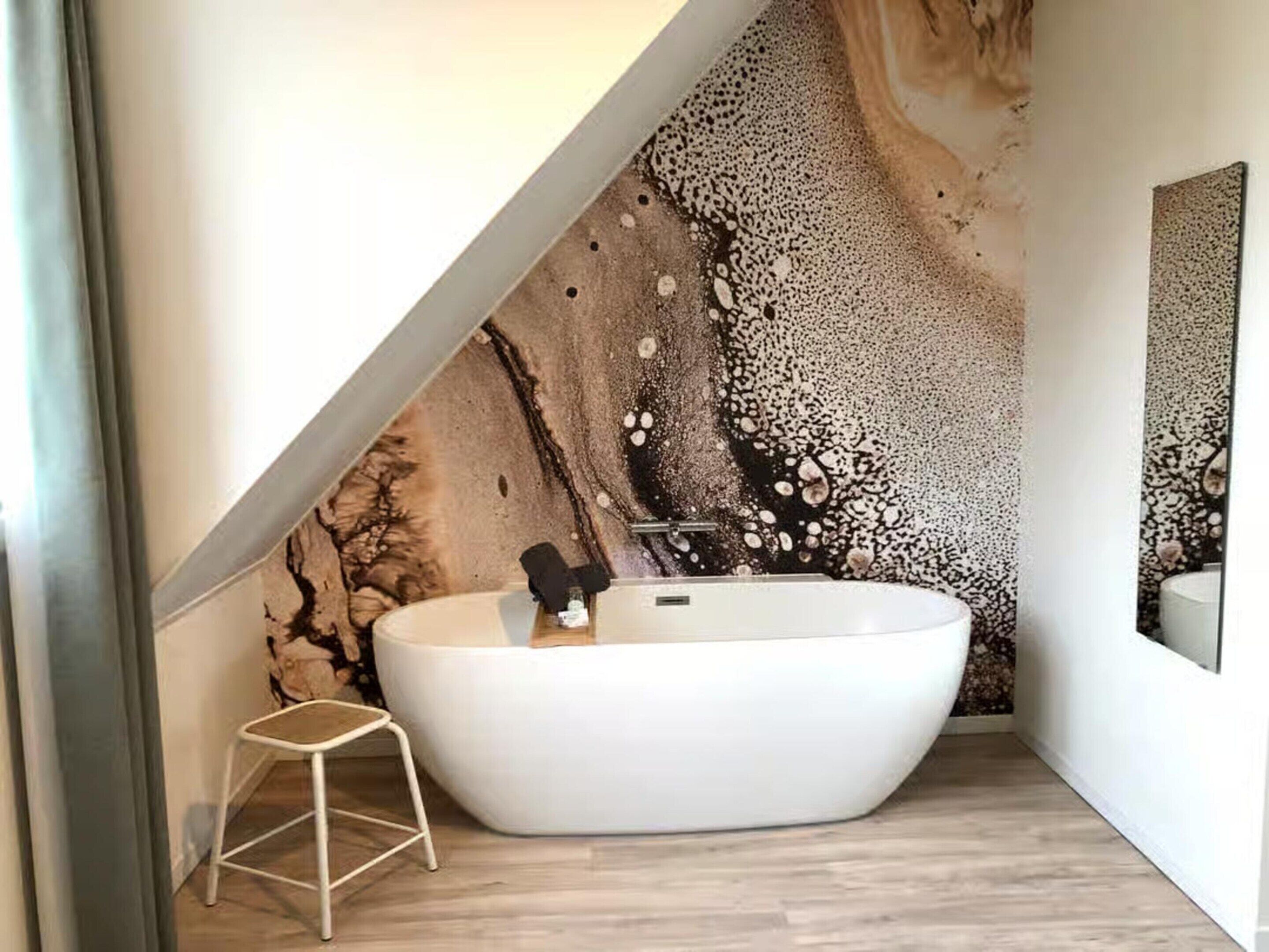 Un baño moderno con una bañera independiente, un taburete pequeño y un mural decorativo.