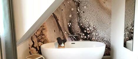 Un baño moderno con una bañera independiente, un taburete pequeño y un mural decorativo.