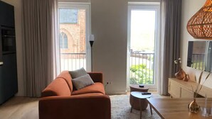 A modern living room with a sofa, a small table, a lamp, and a view of the outside. - Beautiful Lodge in the Center of Zoutelande (Zoutelande)