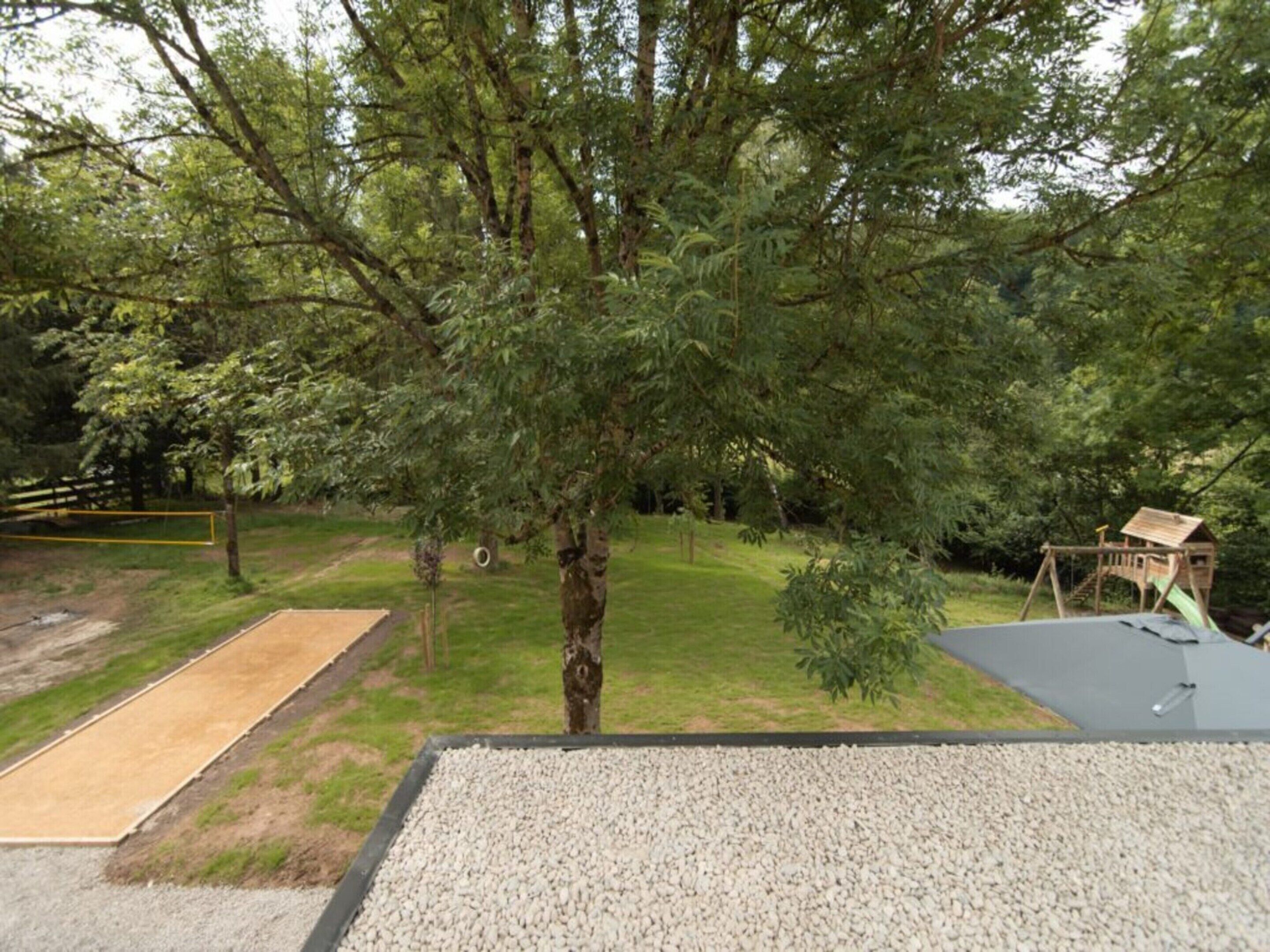 Une aire de jeux avec une balançoire en bois, un petit toboggan et une zone délimitée par une clôture.