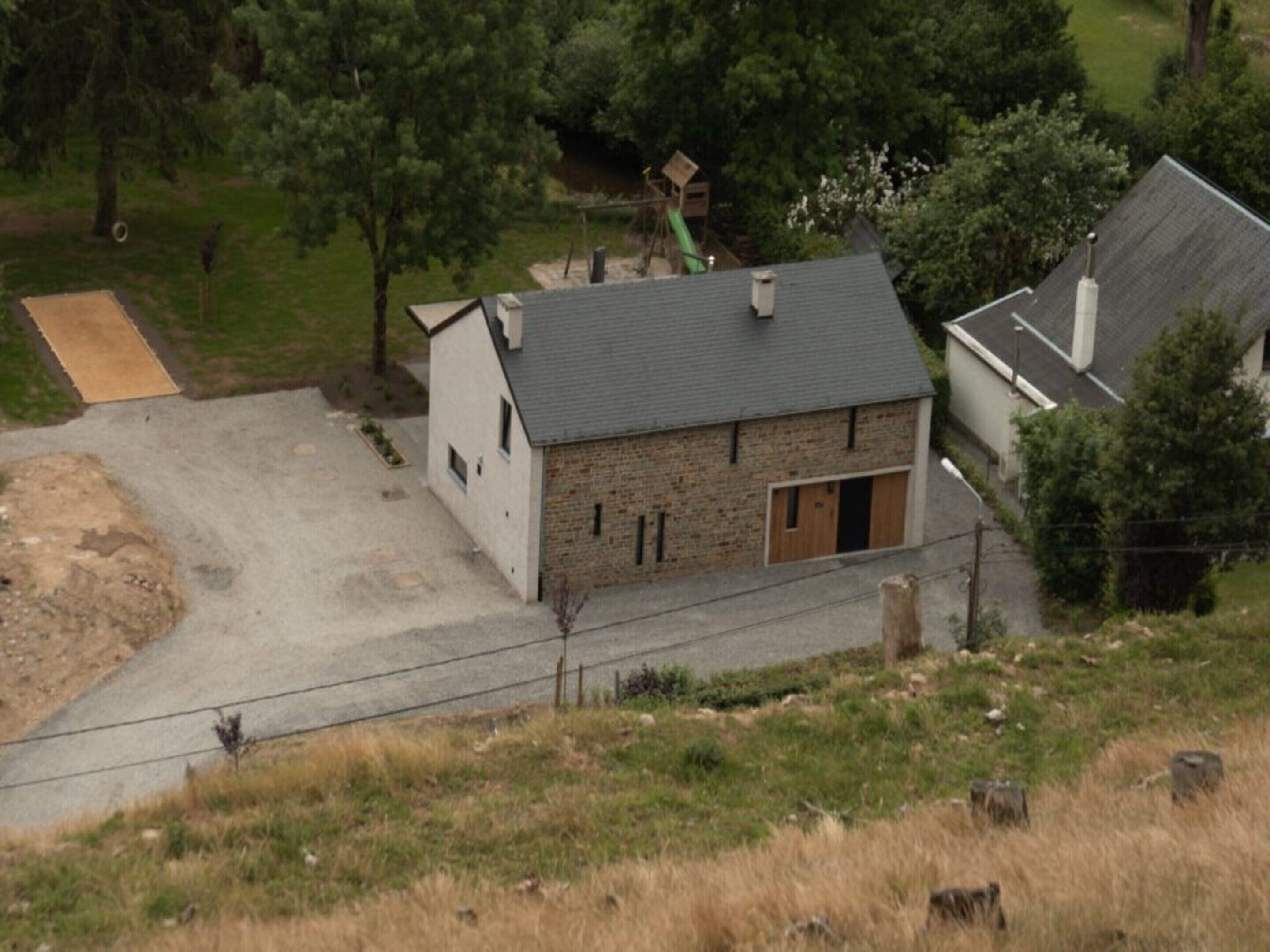 Une maison de campagne à la façade en pierre et au toit gris, entourée d’arbres et bordée d’une allée en gravier.