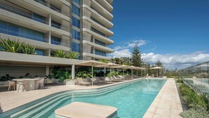 Un hotel moderno con piscina larga, mobiliario exterior y vistas a la ciudad.