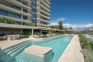 Ein modernes Hotel mit einem langen Schwimmbecken, Sitzgelegenheiten im Freien und Blick auf die Stadt.