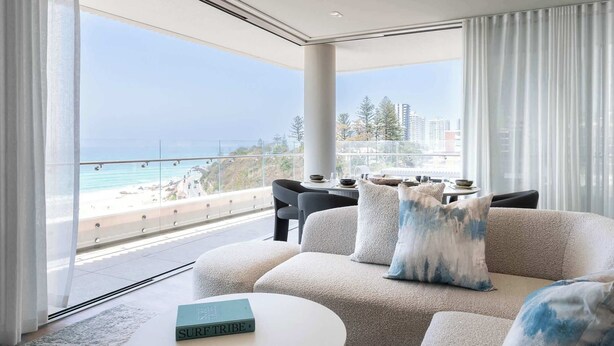 Una sala de estar moderna con un balcón grande con vista a una playa y al horizonte urbano.