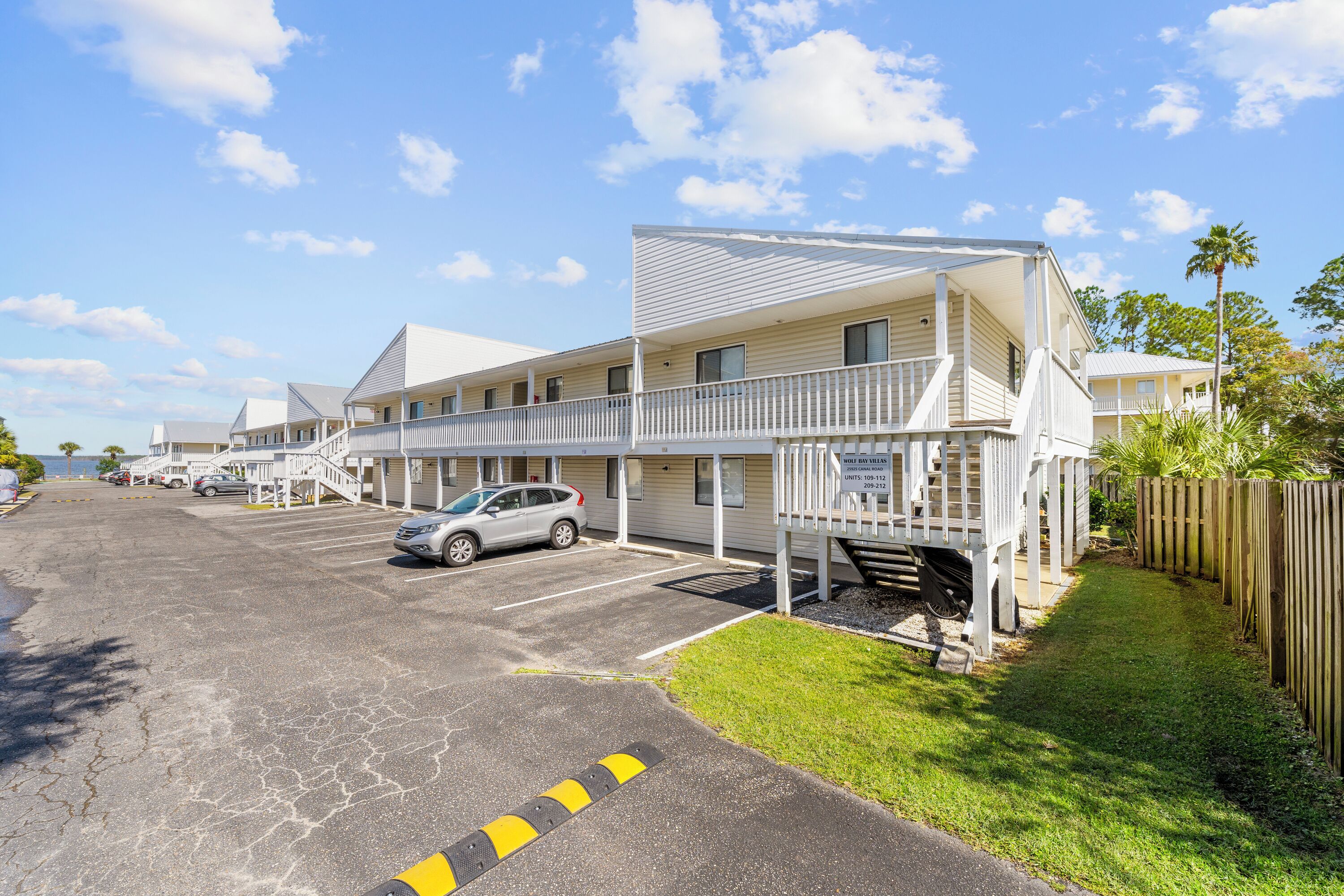 A motel with multiple units, a parking lot, and a grassy area with a wooden fence.