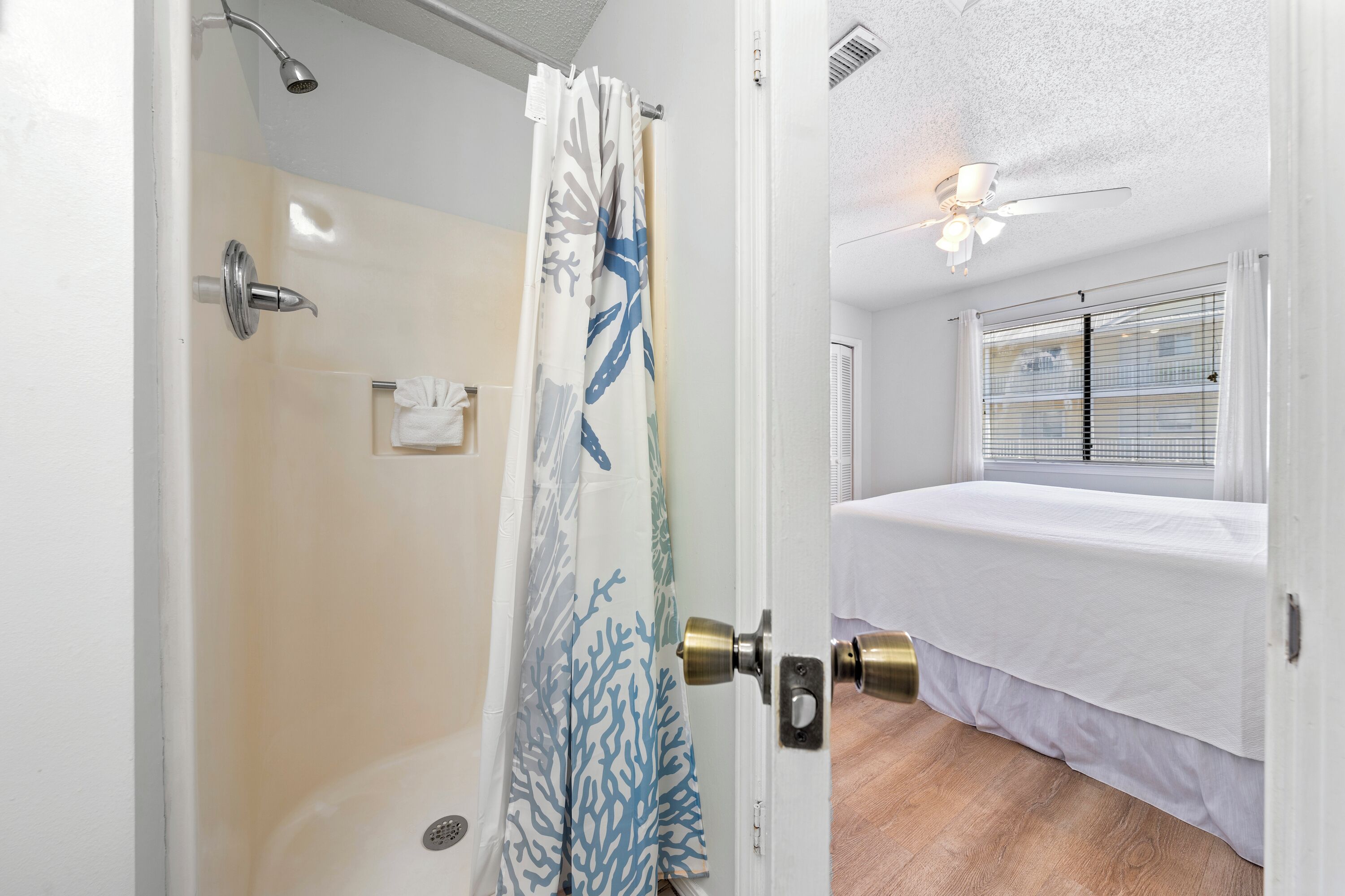 A room with a shower, a bed, and a window with blinds.